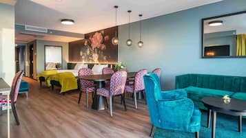 A modern hotel room with a dining area, a sofa, and a large mirror.