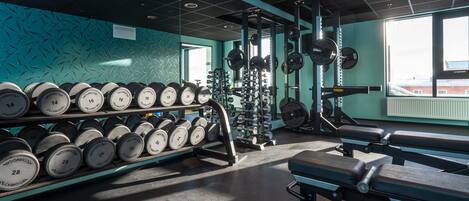 A gym with weightlifting equipment, dumbbells, and a bench.