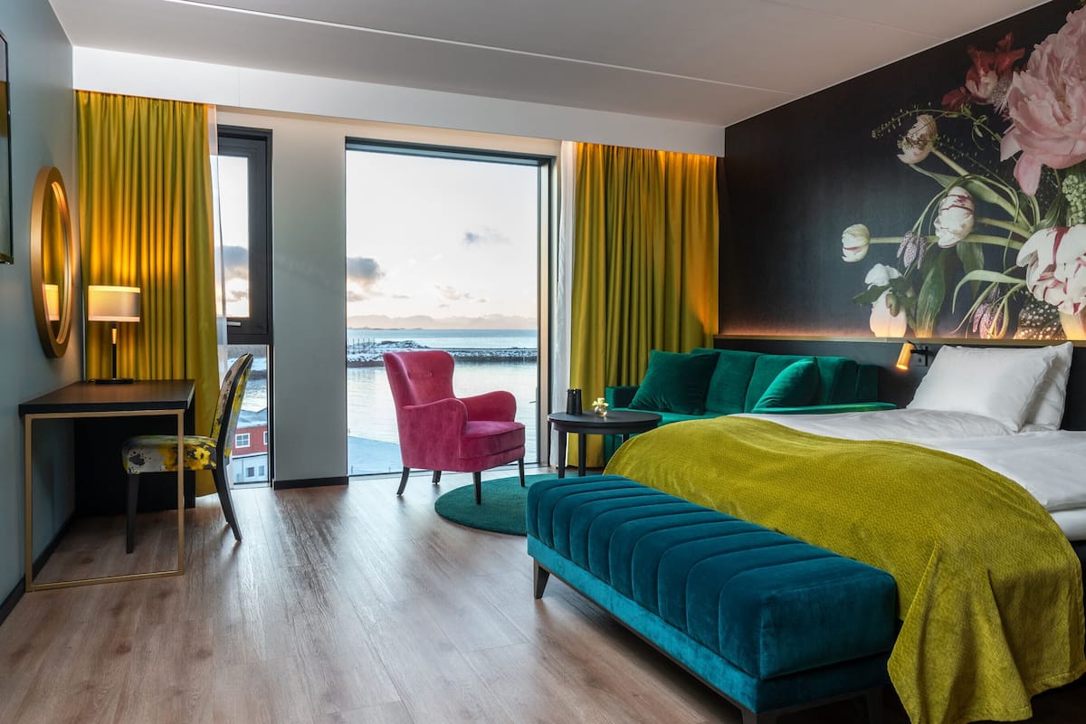 Quarto de hotel com cama, área de estar, escrivaninha e vista para o oceano.