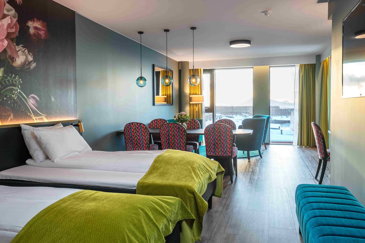 Quarto de hotel com duas camas, uma escrivaninha, cadeiras e vista para a cidade.