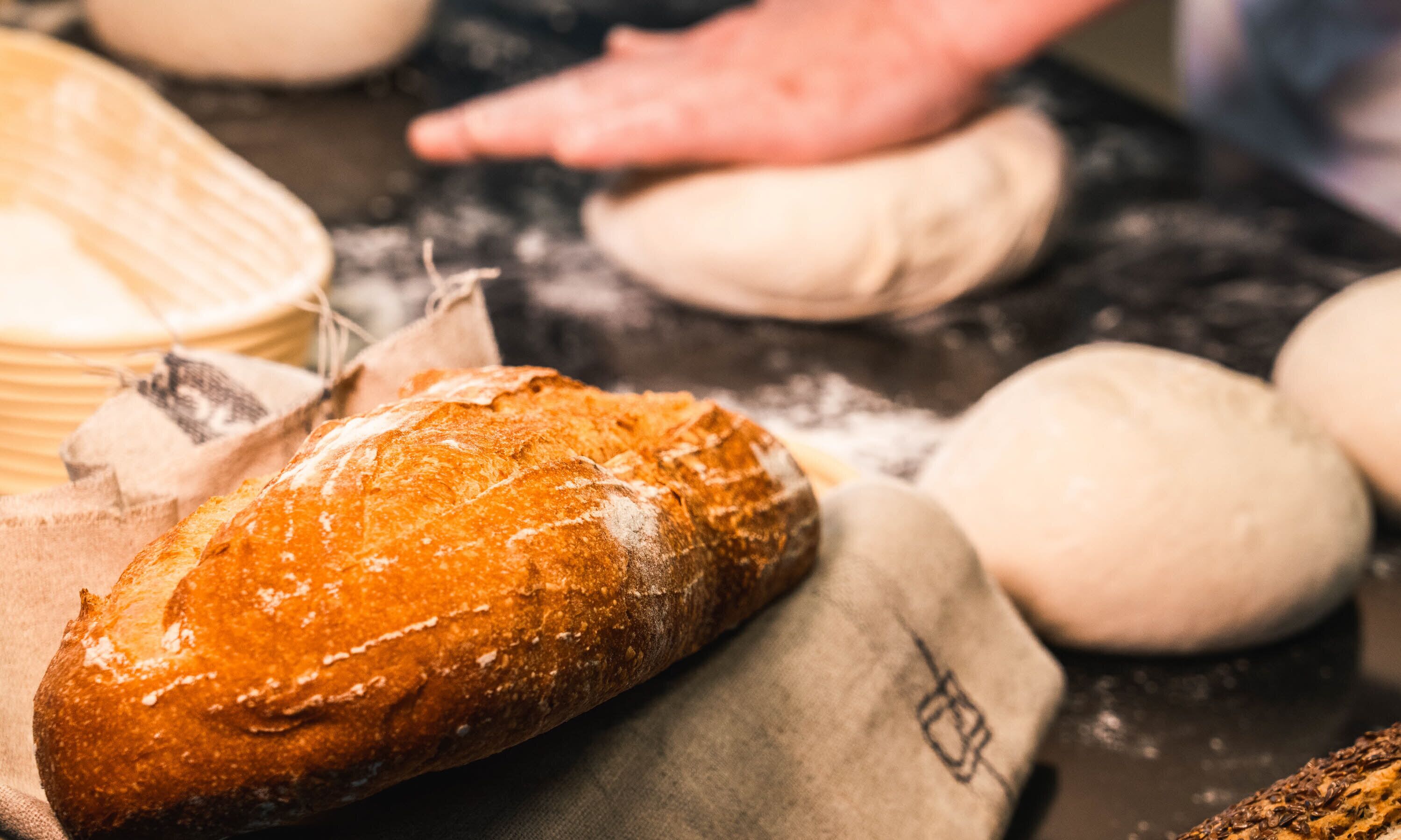 A loaf of bread on a cloth, surrounded by dough balls and a flour-dusted surface.