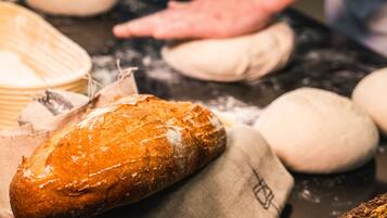 A loaf of bread on a cloth, surrounded by dough balls and a flour-dusted surface.