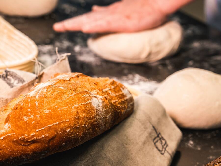 A loaf of bread on a cloth, surrounded by dough balls and a flour-dusted surface.