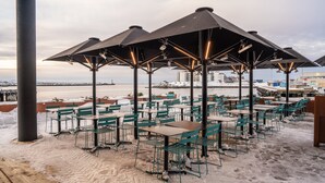 Un espacio al aire libre con mesas y sillas, sombrillas y vista al mar.