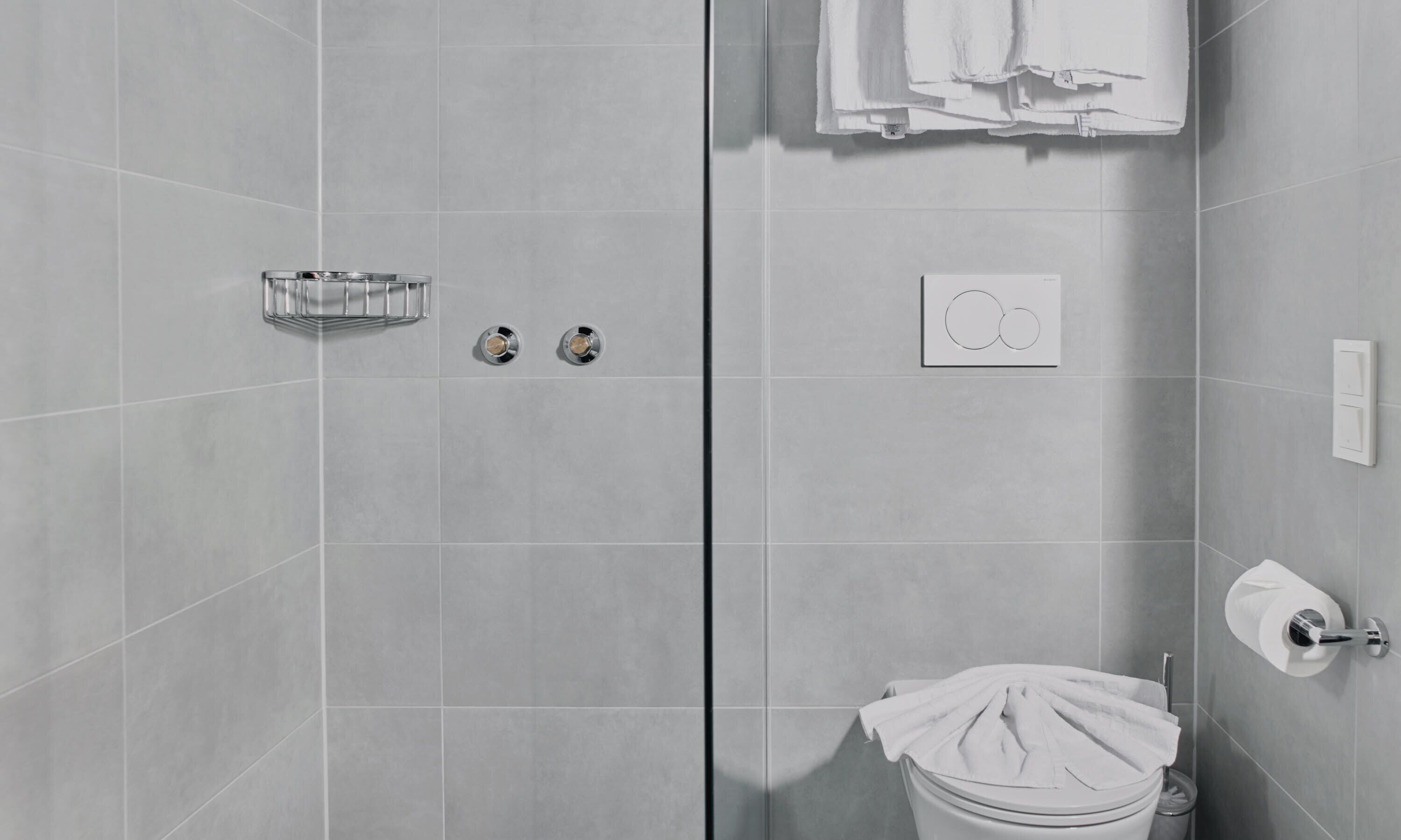 Une salle de bain moderne avec des carreaux gris, des toilettes, un lavabo avec un porte-serviettes et un espace douche.