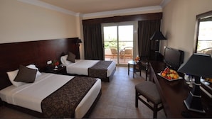Een hotelkamer met twee bedden, een bureau met televisie, een eettafel met fruit en een balkon met tuinmeubilair.