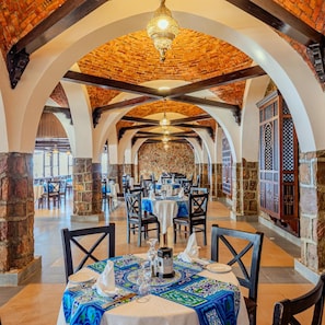 A restaurant with a brick ceiling, stone walls, and a patterned tablecloth. Tables are set with white tablecloths and silverware.
