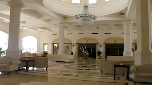 Een ruime lobby met een centrale kroonluchter, grote zuilen en een rond vloerontwerp.