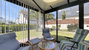 Un patio iluminado por el sol con cerramiento de vidrio, amueblado con sillas de mimbre y una mesa de vidrio, con vista a una zona residencial.