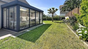 Una casa moderna con un invernadero de cristal, un césped cuidado y un muro de ladrillo.