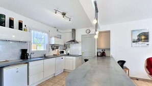 Una cocina moderna con armarios blancos, horno integrado, microondas y cafetera. Hay una ventana con vistas a zonas verdes.