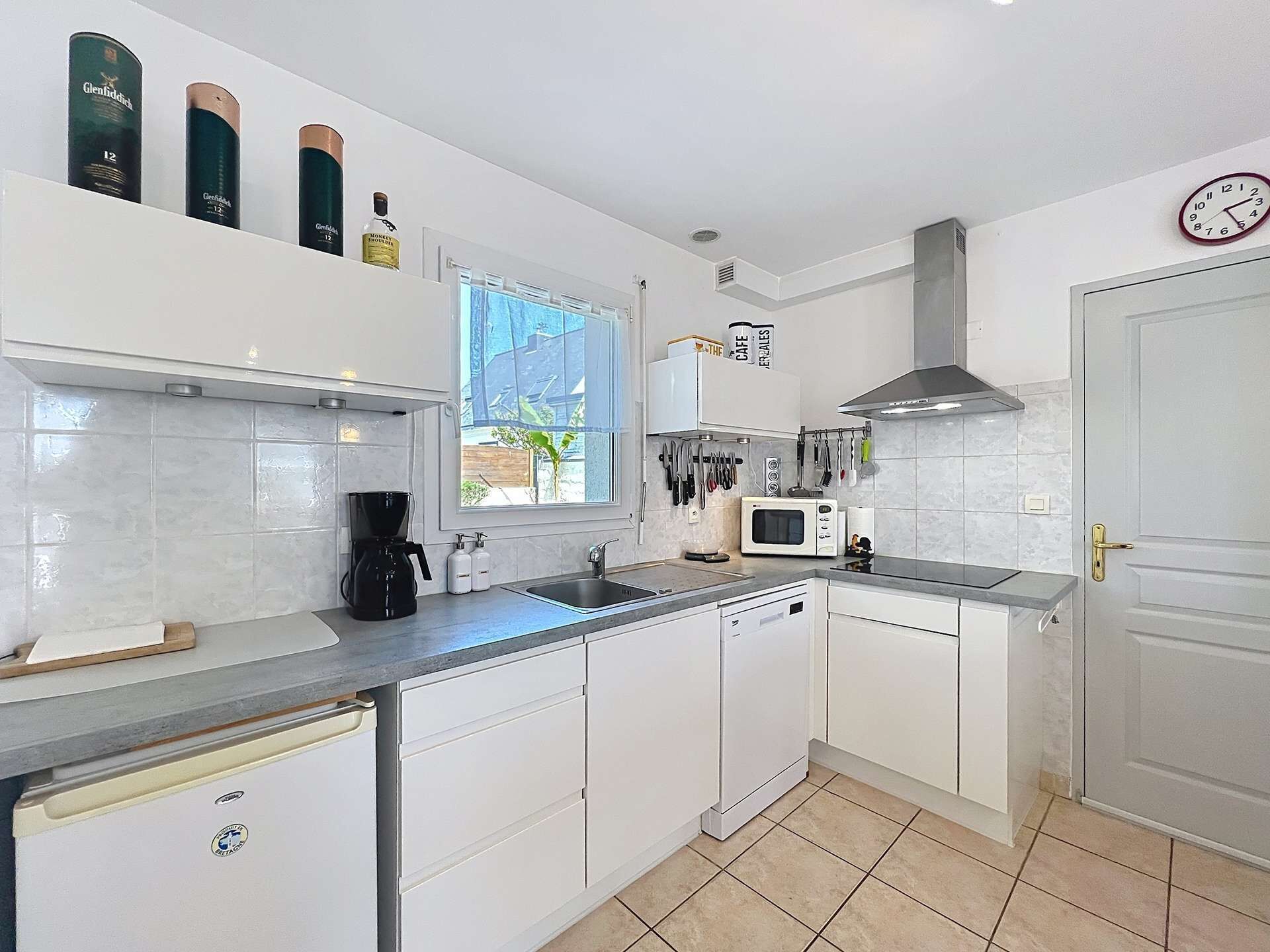 Una cocina moderna con armarios blancos, cafetera, microondas y ventana que proporciona luz natural.