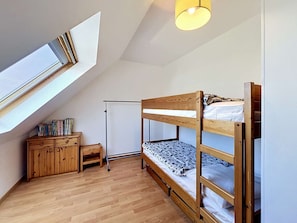 Une chambre de dortoir avec un lit superposé, un bureau avec des livres, une petite armoire et une fenêtre.