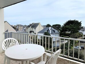 Ein Balkon mit weißem Tisch und Stühlen, der einen Blick auf ein Wohngebiet mit Häusern und geparkten Autos bietet.