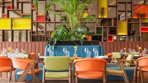 A restaurant with colorful chairs and tables, a central plant, and a wooden wall with shelves. - Emara Ole-sereni (Nairobi)