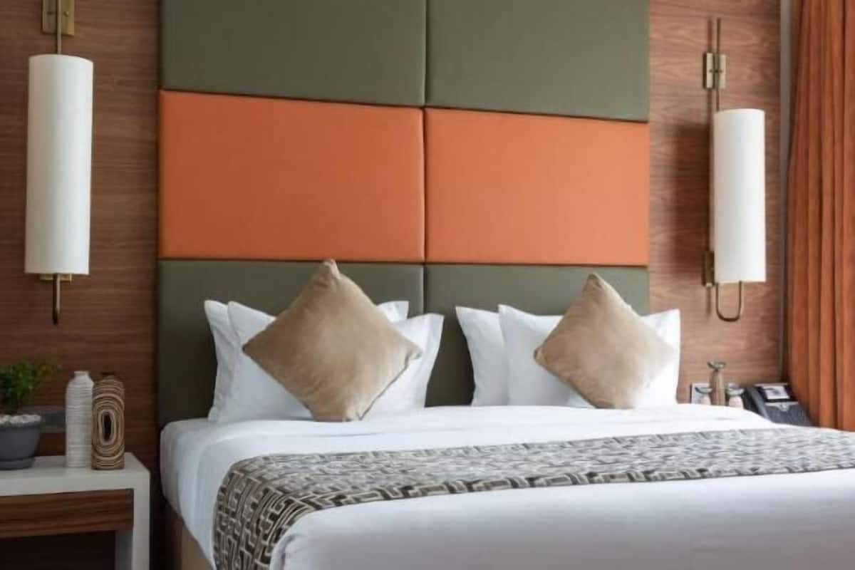 Una habitación de hotel con cama, mesitas de noche, lámpara de pared y cortina.