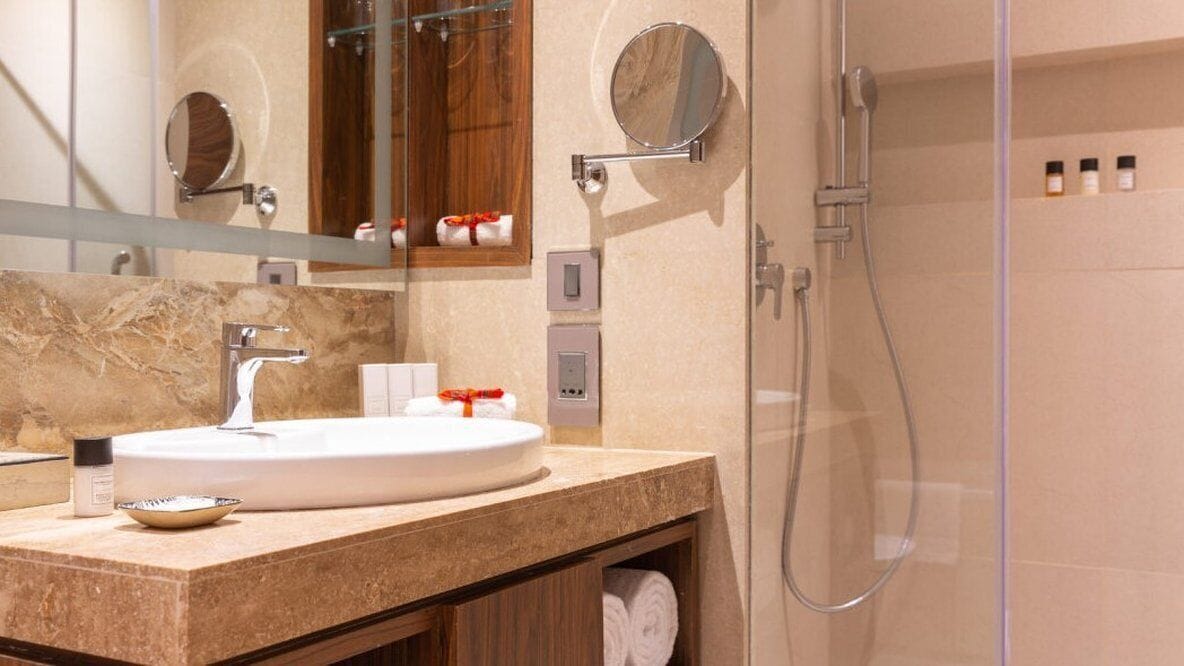 A modern bathroom with a marble sink, a handheld mirror, a glass-enclosed shower, and a towel rack with towels.