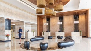 A modern lobby with a marble reception desk, black seating, and a large chandelier. - Emara Ole-sereni (Nairobi)