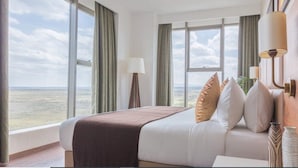 A hotel room with a large bed, two bedside lamps, a view of the landscape, and a window with curtains. - Emara Ole-sereni (Nairobi)