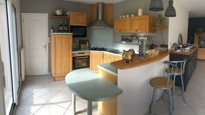 Una cocina con armarios de madera, una isla central con taburetes, microondas, estufa y lámparas colgantes.