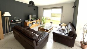 Una sala de estar moderna con una pared oscura, un mueble de entretenimiento de madera, un sofá de cuero marrón, una mesa de centro de vidrio y una planta en maceta.