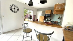 Una cocina moderna con una isla central, dos taburetes de bar, armarios de madera, un microondas y un reloj en la pared.