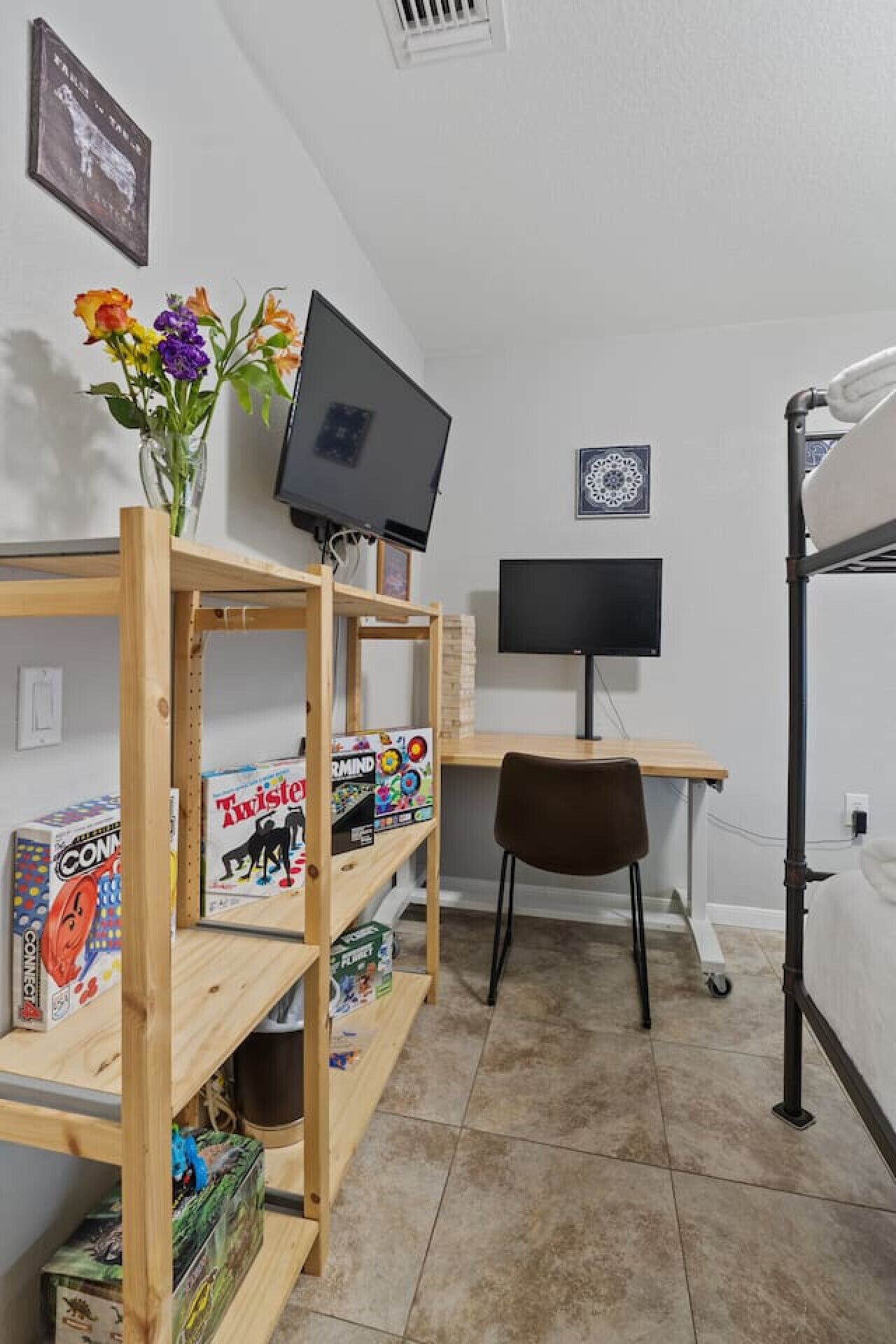 A compact room with a bunk bed, a desk with a computer, and shelves with board games.