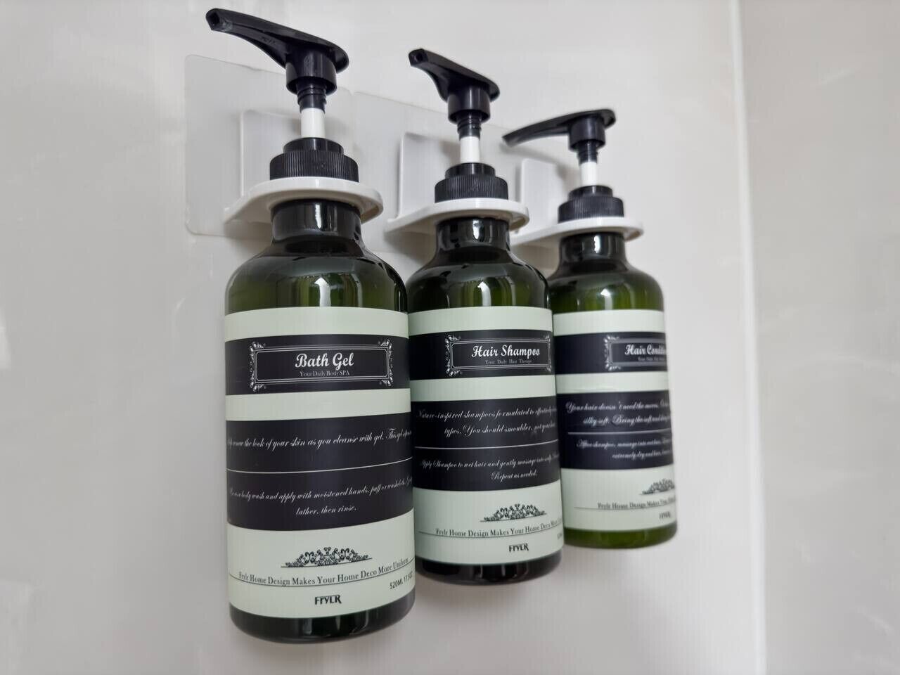 Tres botellas de productos de baño con dosificadores, etiquetadas como Gel de Baño, Champú para el Cabello y Acondicionador para el Cabello, sobre una superficie blanca.
