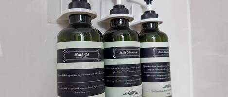 Trois flacons de produits de bain dotés de pompes, étiquetés « gel douche », « shampooing » et « après-shampooing », sont présentés sur une surface blanche.