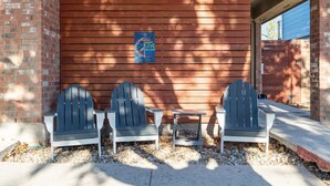 Ein Backsteinhaus mit einer Holzschrankenwand, zwei Adirondack-Stühlen, einem kleinen Tisch und einem Schild, das Frieden, Gleichheit, Liebe und Inklusion bewirbt.