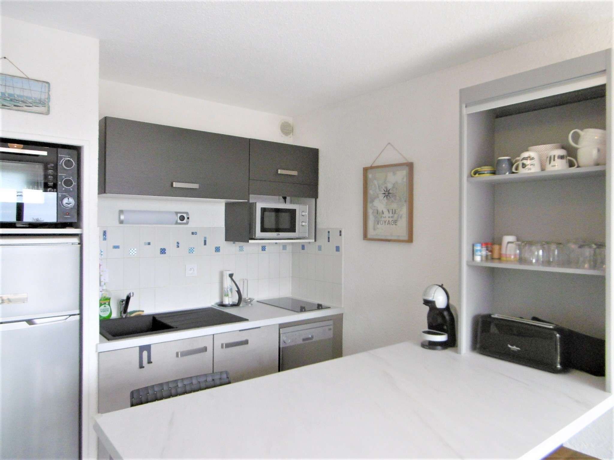 A modern kitchen with a microwave, oven, and dishwasher. There is a coffee maker and a framed picture on the wall.