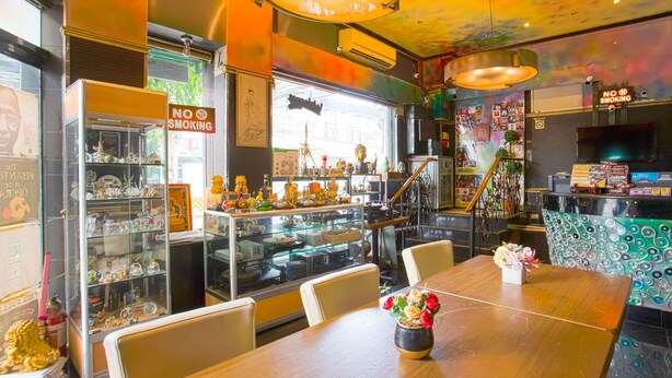 Interior de restaurante con un cartel de 'No Fumar', una vitrina con productos alimenticios y una mesa de madera con un jarrón de flores.