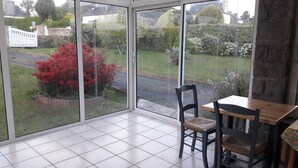 Habitación con un gran ventanal que da a un jardín. En el interior, una mesa de madera y dos sillas.