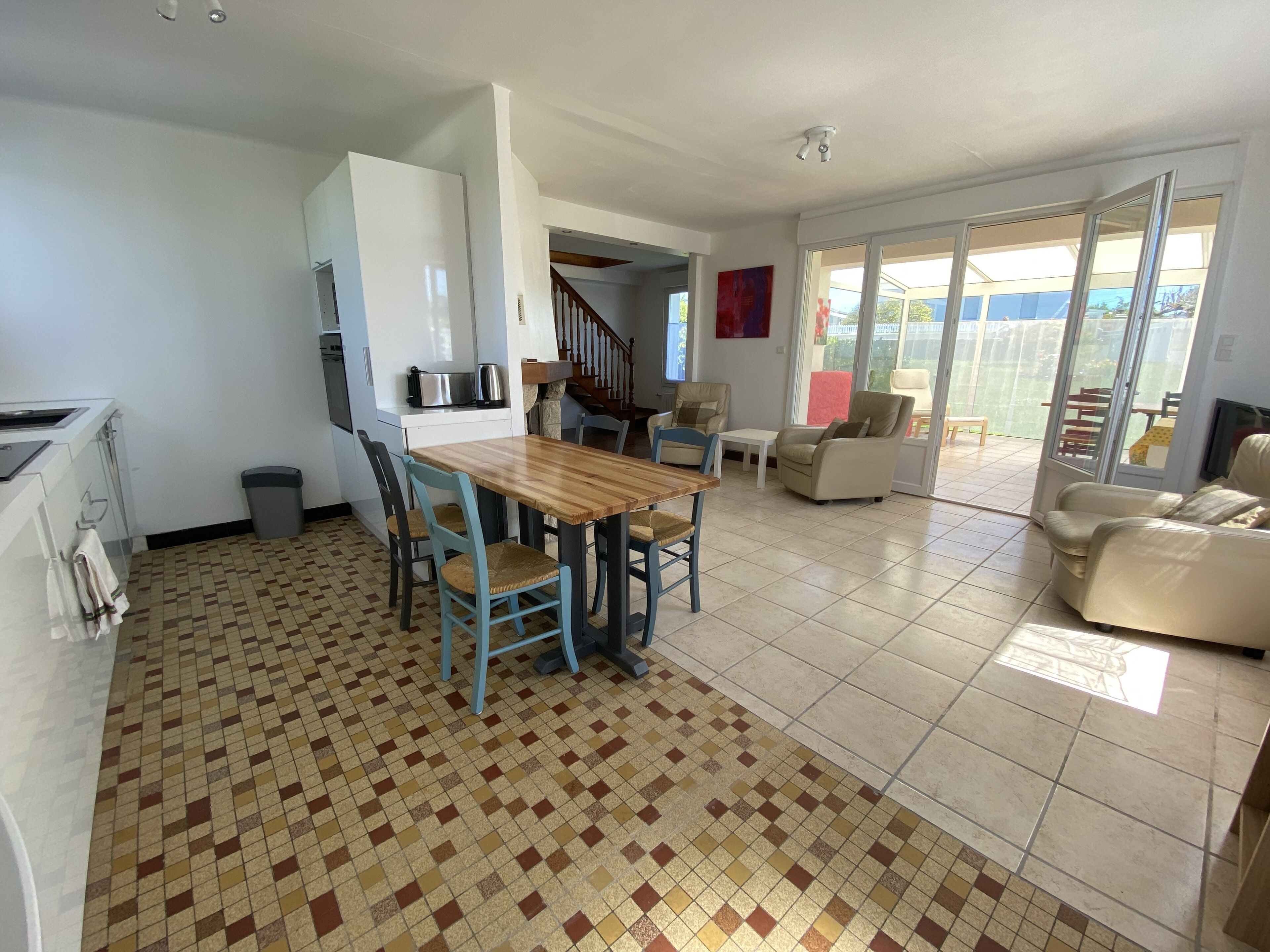 Amplia sala de estar con suelo de baldosas, una mesa de comedor de madera y varias opciones de asientos, incluyendo un sofá y sillas.