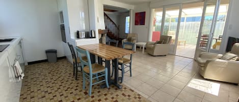 A spacious living area with a tiled floor, a wooden dining table, and multiple seating options including a sofa and chairs.