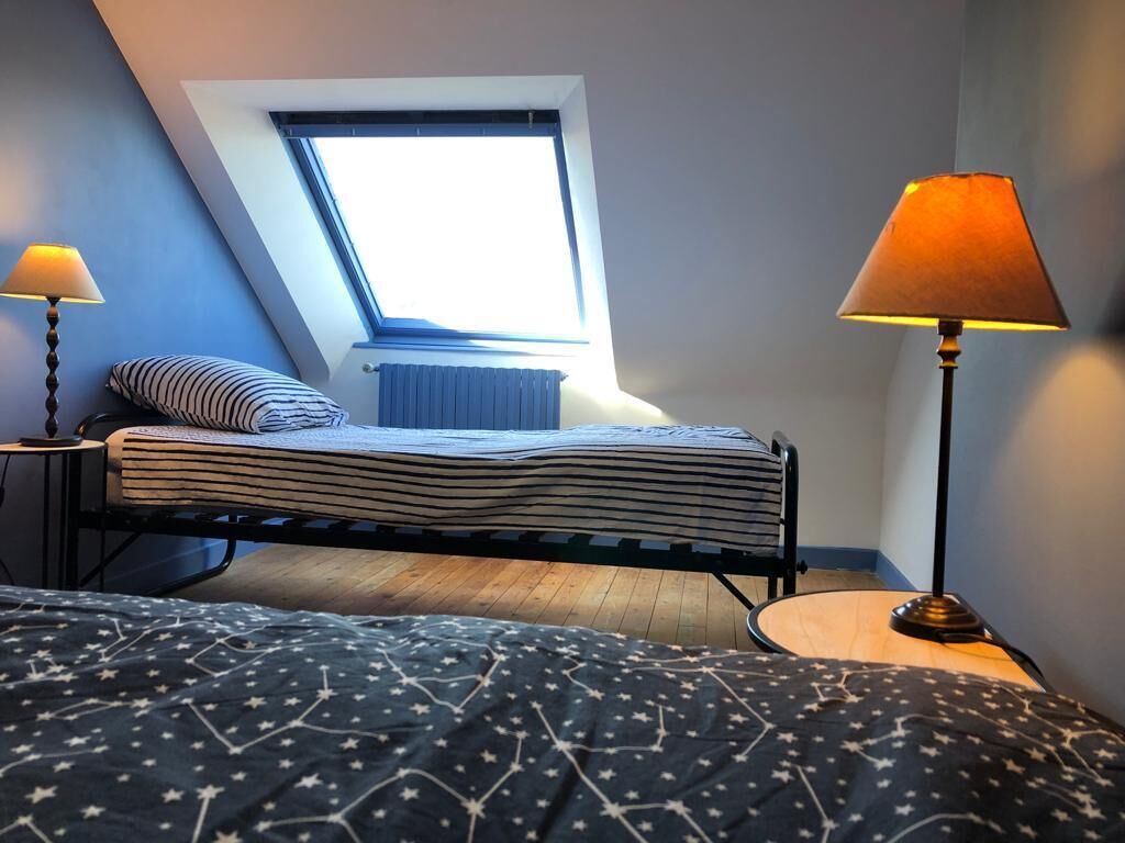 A bedroom with a skylight, a bed with a striped blanket, a bedside lamp, and a star-patterned blanket.