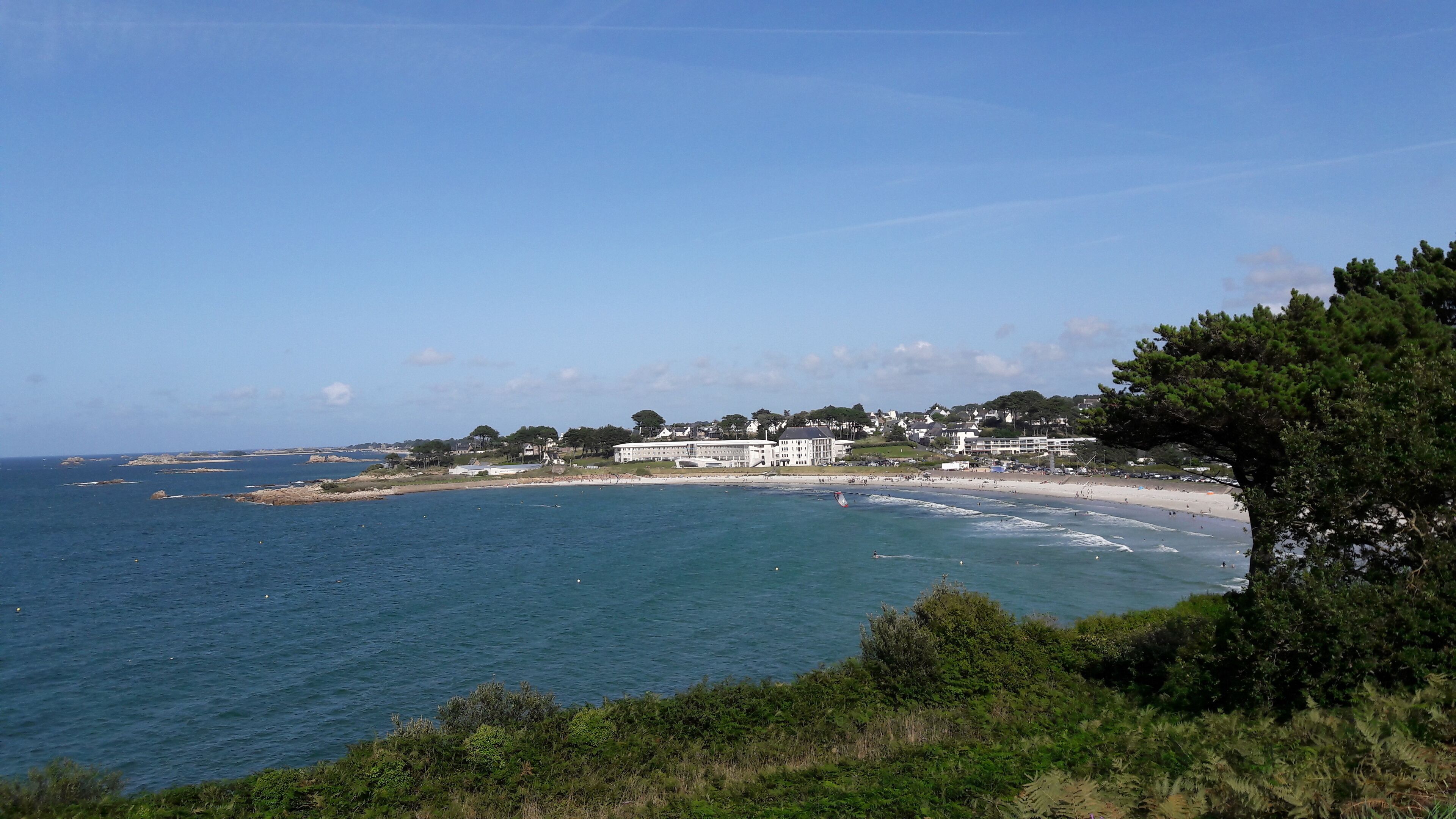 A coastal view with a large building, beach, and clear sky.