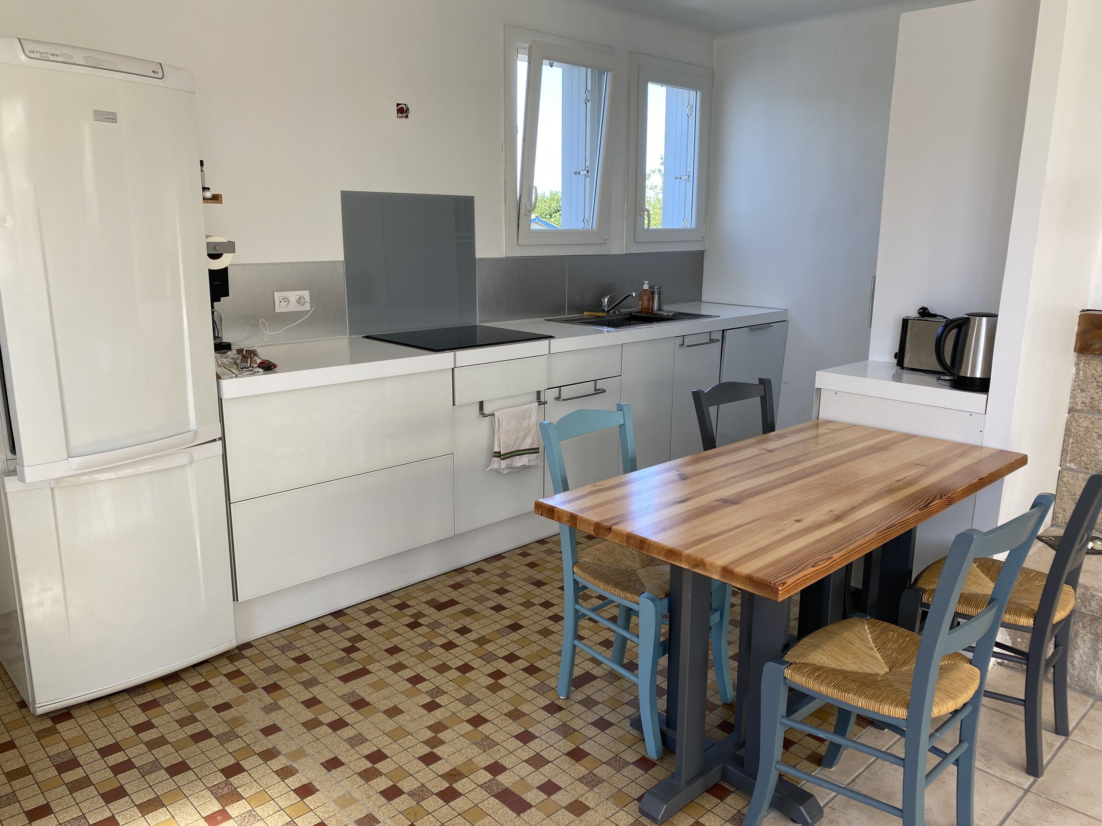 A compact kitchen with white cabinets, a wooden table, and blue chairs.