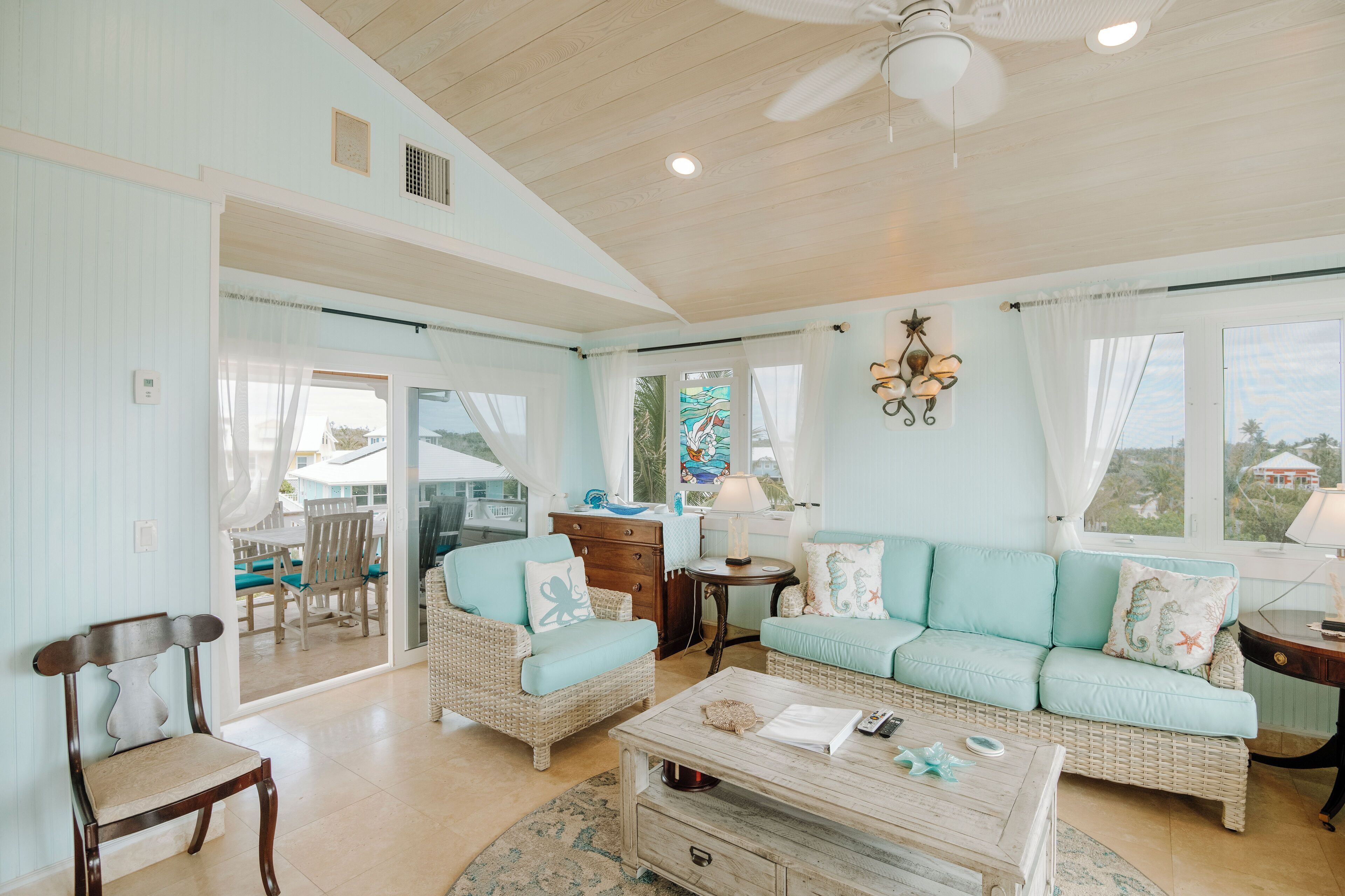 Un salón amplio con una decoración en tonos azul claro, muebles de mimbre y vistas al exterior.