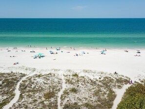 A beach with white sand, clear turquoise water, and sparse vegetation.