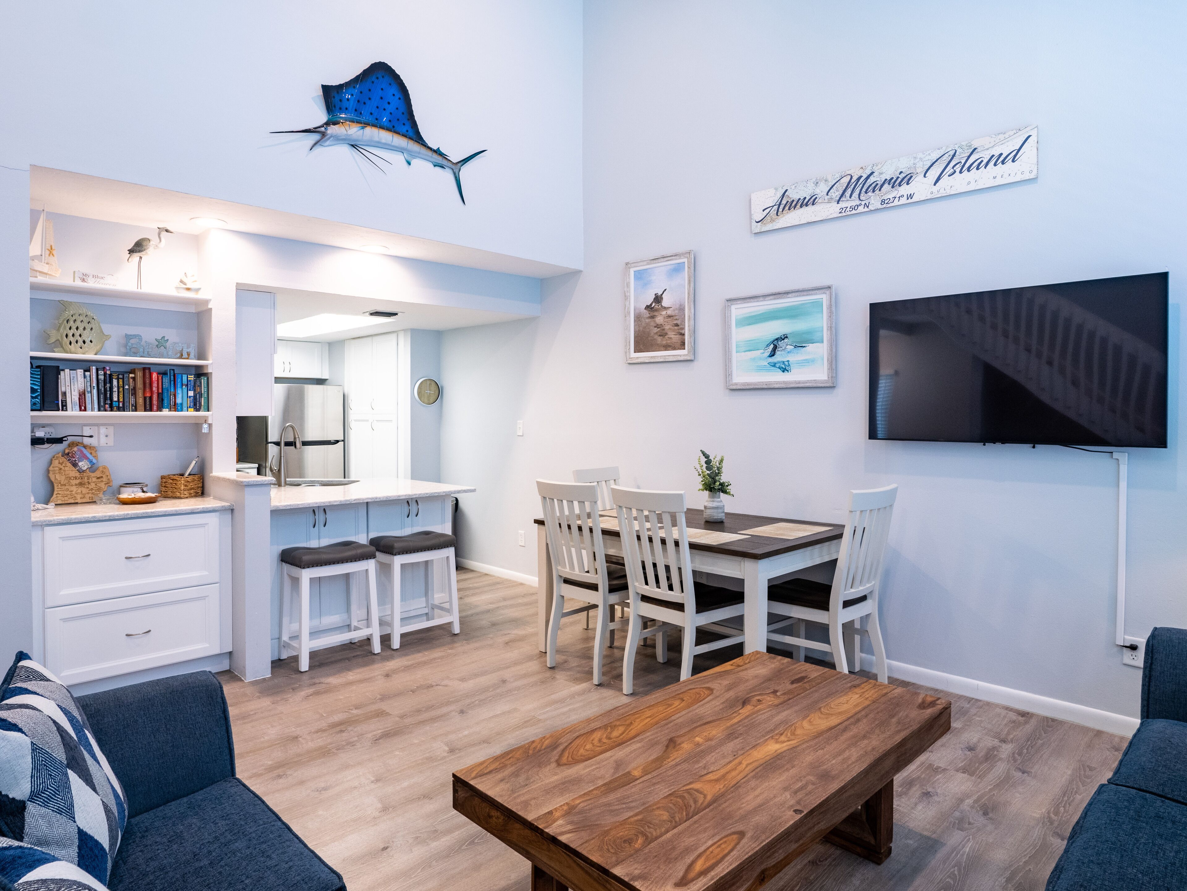 A modern kitchen with white cabinets, a central island, and a dining area with white chairs and a wooden table.