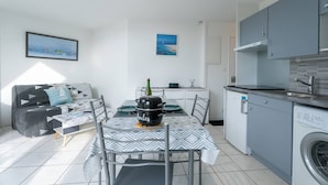 Un espace de vie compact comprenant un coin repas, une kitchenette et un canapé recouvert d’un tissu à motifs géométriques.