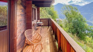 Une terrasse en bois avec une chaise en osier et une table, offrant une vue sur un paysage montagneux.