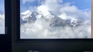 Une pièce dotée d’une grande fenêtre donnant sur une chaîne de montagnes aux sommets enneigés et aux nuages.