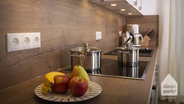 Une cuisine moderne avec des meubles en bois, une cuisinière en acier inoxydable et un panier de fruits posé sur le plan de travail.