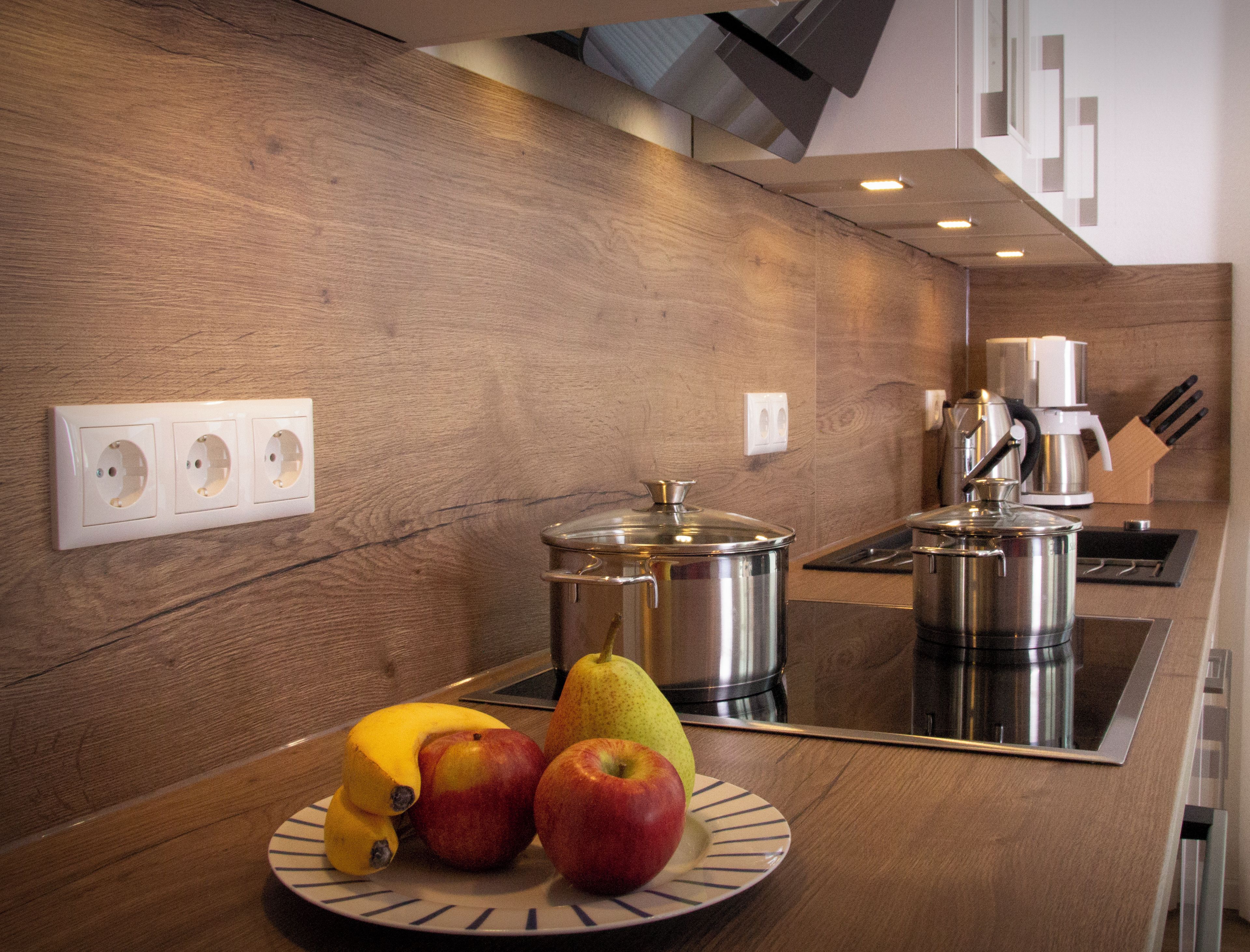 Una cocina moderna con armarios de madera, una estufa de acero inoxidable y un frutero sobre la encimera.