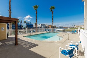 A pool area with a clear blue pool, palm trees, and lounge chairs. - Waterfront Condo | Pool Access & Stunning Views (Corpus Christi)