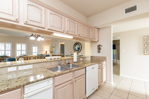 A modern kitchen with granite countertops, a dishwasher, and light-colored cabinetry. - Waterfront Condo | Pool Access & Stunning Views (Corpus Christi)