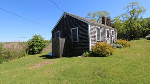 A small, single-story house with a sloped roof, a chimney, and a fenced yard.
