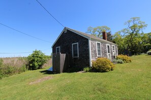 A small, single-story house with a sloped roof, a chimney, and a fenced yard.